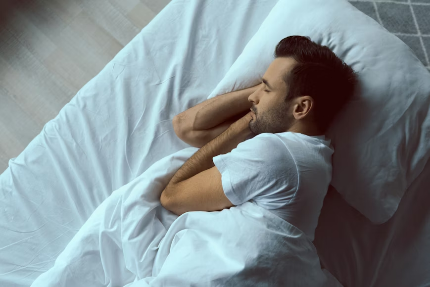 foto de cima de homem dormindo de lado em uma cama