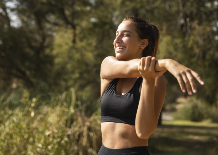 foto de uma mulher alongando o braço direto e sorrindo no parque