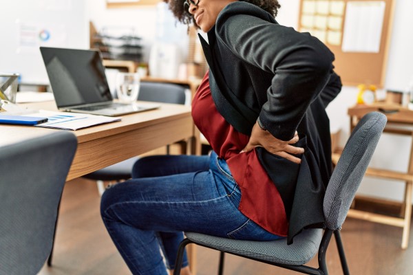 mulher sentada no escritório do trabalho com dor nas costas